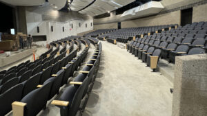 A long shot of the auditorium; rows of 650 blue chairs face a stage, and the sound-proofed walls and ceiling tiles are captured, too.