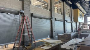 Three gray industrial vertical sliding doors are pictures, as is a ladder. They are the interior doors adjoining the soon-to-be cafeteria and commons. 