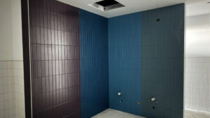 This is the bathroom tiling. There is a wall of slim brown tiles adjoined to a wall corner covered with slim blue tiles beside a wall of green tiles.