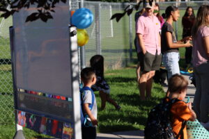 A preschooler poses for a picture in front of a sign with balloons.