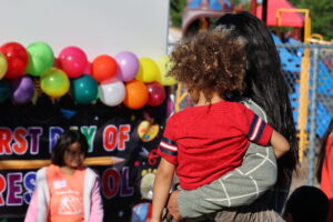 A mother holds her daughter in front of the First Day of Preschool sign.