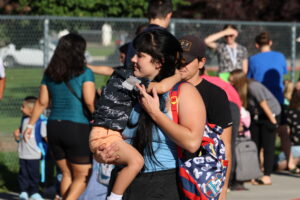 A mother carries her son in a line, waiting for school to start.