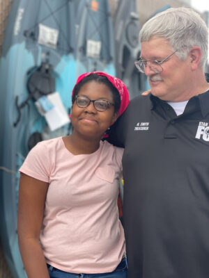 An officer gives a young female student a side hug as the young woman beams at the camera.