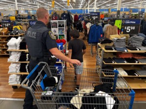 An officer and a boy shop for shirts in the aisles of Walmart.