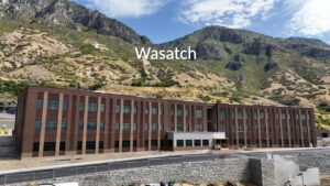 Wasatch Elementary School's red brick facade and exterior with the mountain range in the background. A captioned word, "Wasatch," hovers above the school.