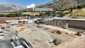 Timpview High School's southwest bulldozed parking lot is shown from a long angle, with a mountain range in the background. A captioned word, "Timpview," hovers above the school.