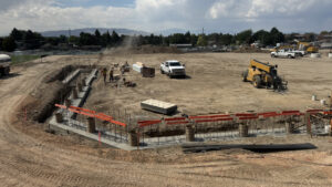 A long, high-angled shot of the sotball dug-out rebar, with a white truck in the background. Behind the rebar sits a bundle of plywood.