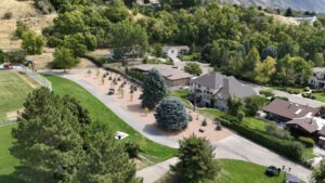 A drone shot of the South Exterior walkway near the Football field. There is sod planted near the new sidewalk, as well as an island between the sidewalk and the adjoining neighborhood houses. The island contains red stone and planted trees.