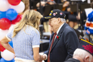 The mayor is shaking hands with a veteran wearing a veteran's hat.