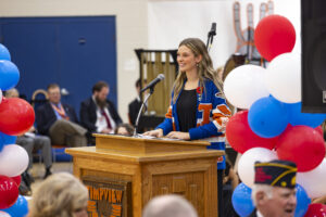 A student council member is standing and speaking into a microphone behind a pulpit.