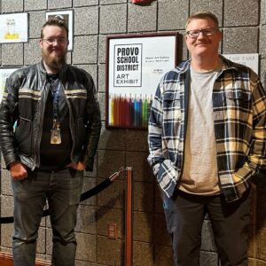 Two Teachers stood next to a poster at the Covey Arts Center. The post reads, "Provo School District Art Exhibit."