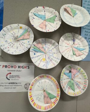 Paper plate cutouts with inscriptions hang on a wall.