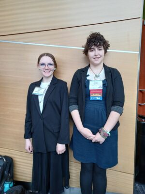 Two students wearing business casual stand in front of a wood wall backdrop.