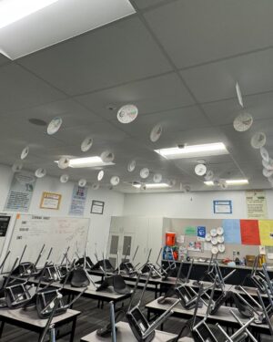 Paper plate cutouts with inscriptions hang on strings from the classroom ceiling.