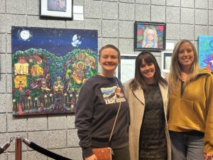 A student, Provo High Arts Teacher Linsday Ruiz, and Provo High Principal stand in front of a portrait painting of a moony sky with green trees and a lit gate.