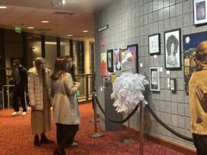 Two women stand behind a velvet rope; they are looking at a dress with ruffled lace.