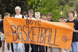 Young boys hold a large orange banner which reads, "Boys Basketball."