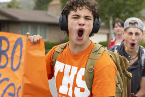A boy in an orange shirt is yelling excitedly at the camera.
