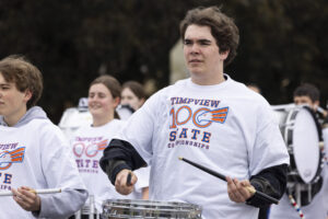 A boy in a white shirt with text reading, "Timpview 100 State" plays the drums.