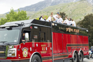 A group of students in white t-shirts are sitting atop a fire truck.